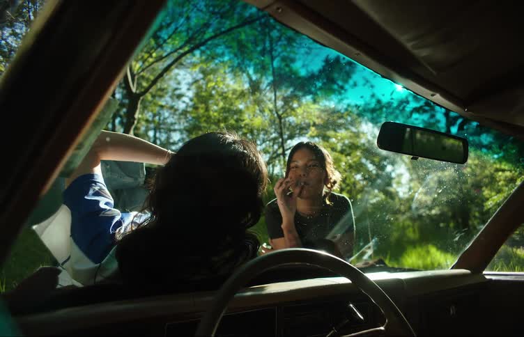 Two girls laying on the hood of a car smoking