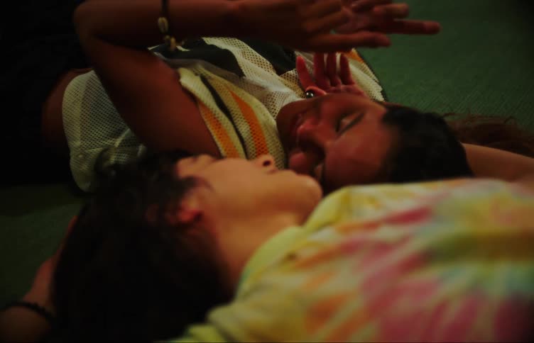 Two young women lying on the living room rug looking at each other and holding their hands together