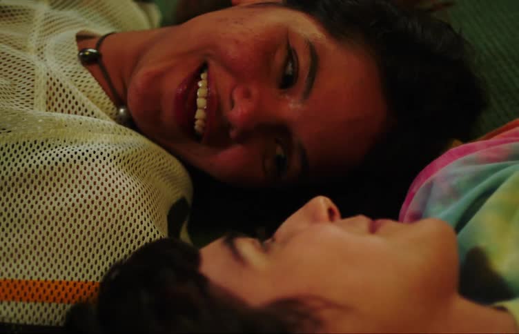 Two young women lying on the carpet looking at each other face to face and laughing