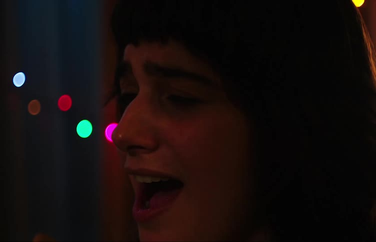 Two teenage girls singing in a dimly lit room with colorful lights