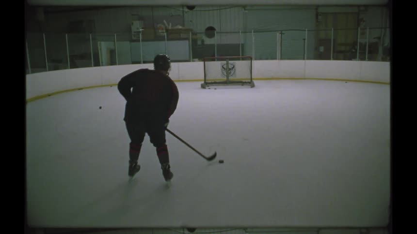 A man skates shooting a puck into an empty net