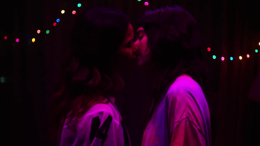 Young women dancing together indoors at night share a kiss