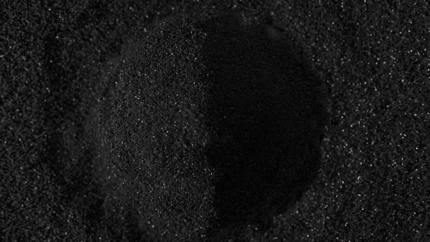 Glittery black sand bursts outward before falling in again
