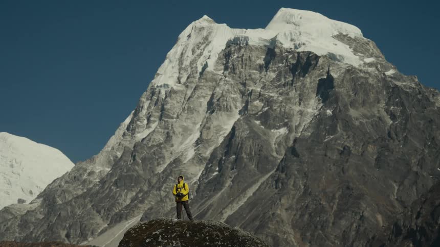 Man above a rock on a cliff with mountain range around him covered in snow