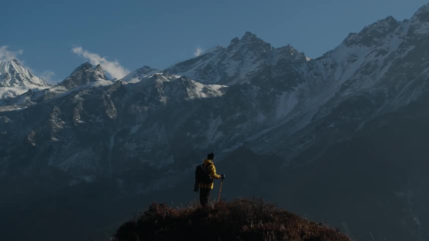 Man with hiking equipment on the peak of a hill on a cliff and with a natural view of snowy mountain ranges