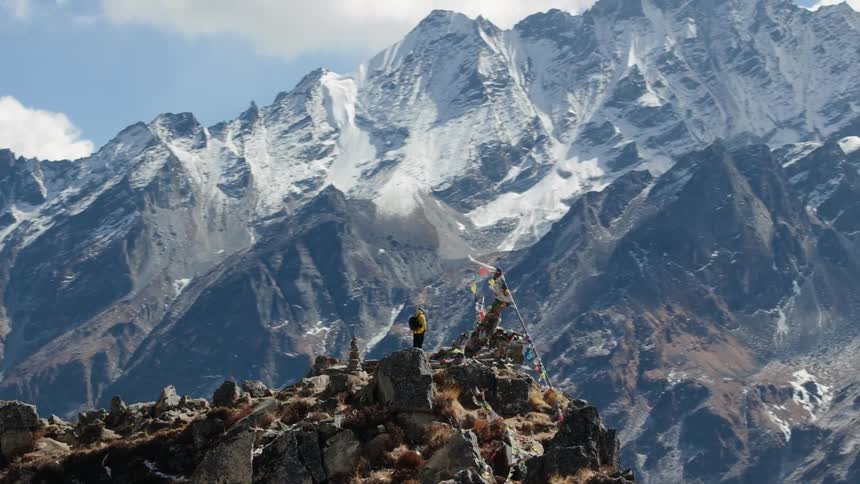 Aerial shot of a man on the peak of a cliff with a stunning view of snowy mountains
