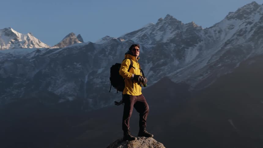 Man standing on a rock on a cliff with a view of snowy mountains