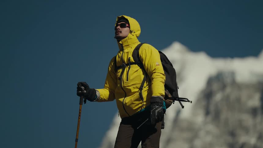 A hiker stands on a mountain gazing at snowcapped peaks in the distance