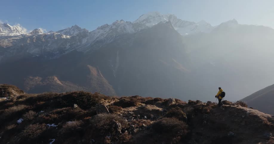 A person is walking on a mountain top in a mountainous region and in strong sunlight
