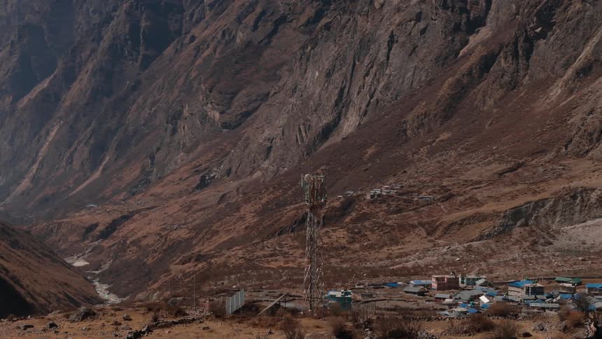 Aerial scene of a large signal and power transmission tower on a hill in a natural region with mountains and a village around it