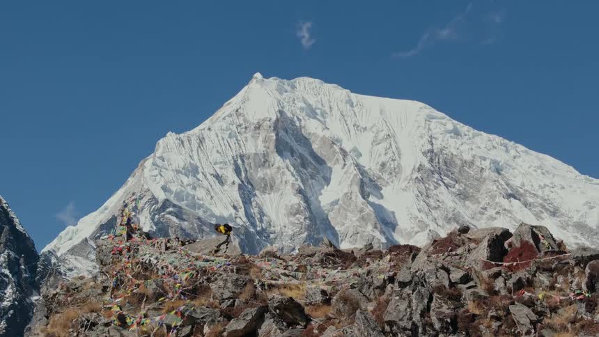 Panorama of a man walking on a cliff surrounded by snowy mountains during the day