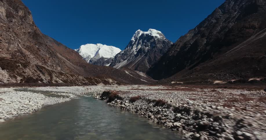 Shallow river amidst rocks and surrounded by rocky mountains on a winter day with a blue cloudless sky