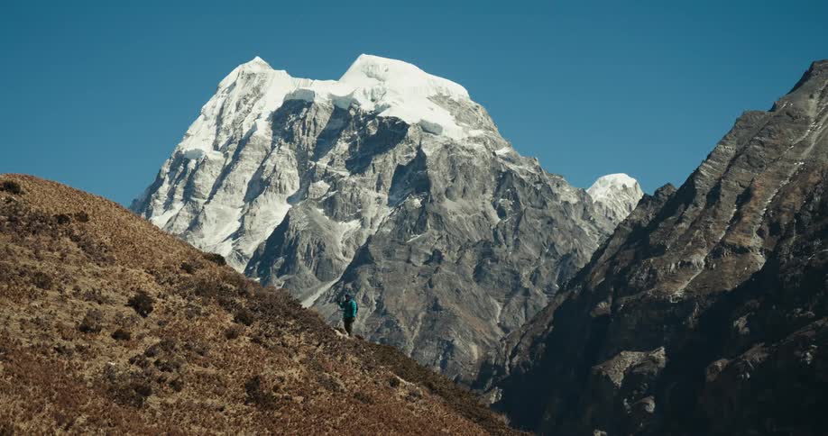A hiker climbs a grassy mountain with a large snowcapped mountain looming behind