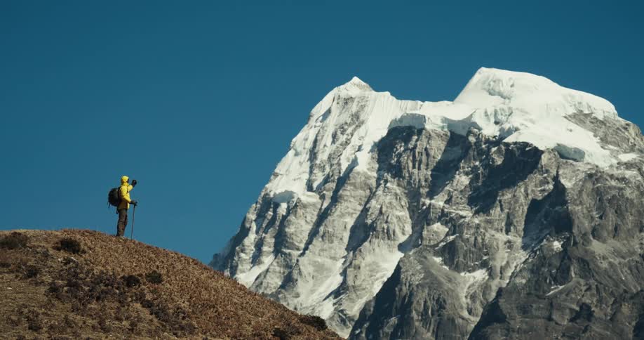 A hiker stands on a mountain ridge gazing at snowcapped peaks in the distance