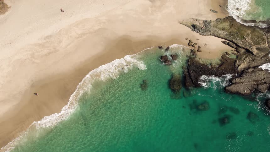 Aerial panorama of a turquoise beach with clear sand and rocks around