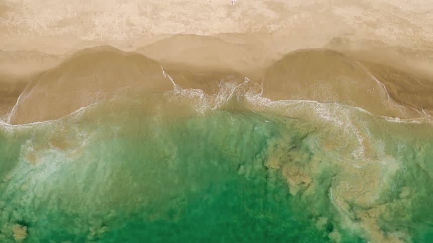 Birds eye view of turquoise beach waves crashing onto sandy shoreline