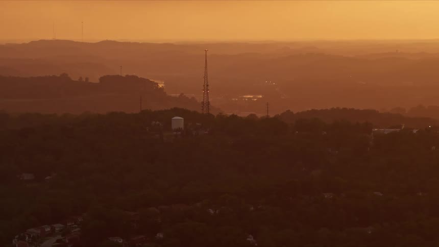 Aerial panorama of a transmission tower on the peak of a hill with residential neighborhoods around it on a reddish morning sky