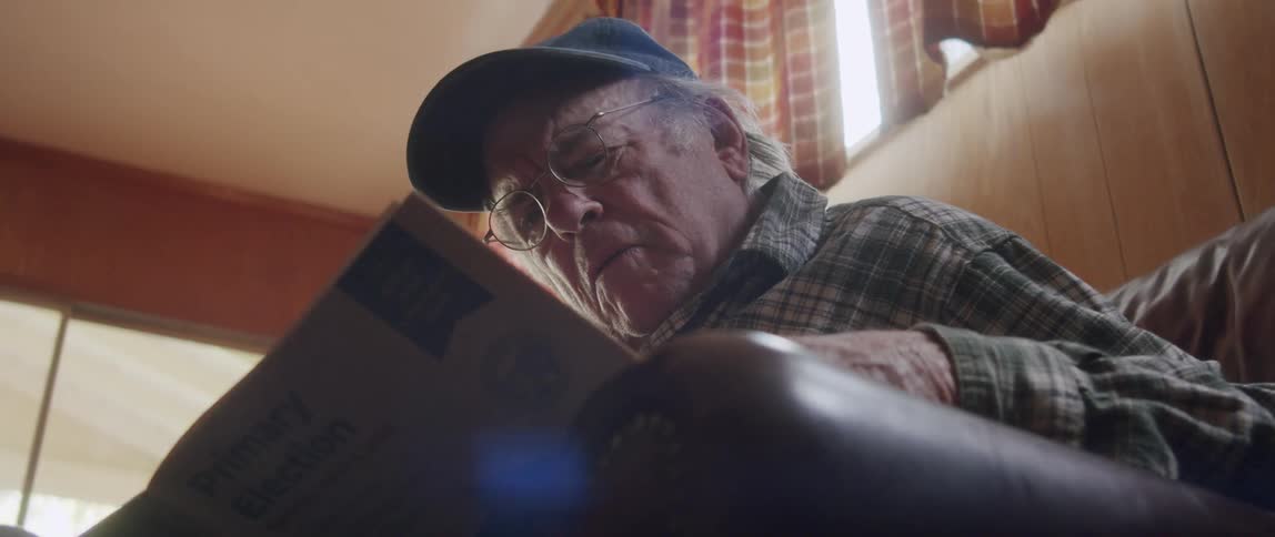 Elderly man carefully reading the newspaper while sitting in the room
