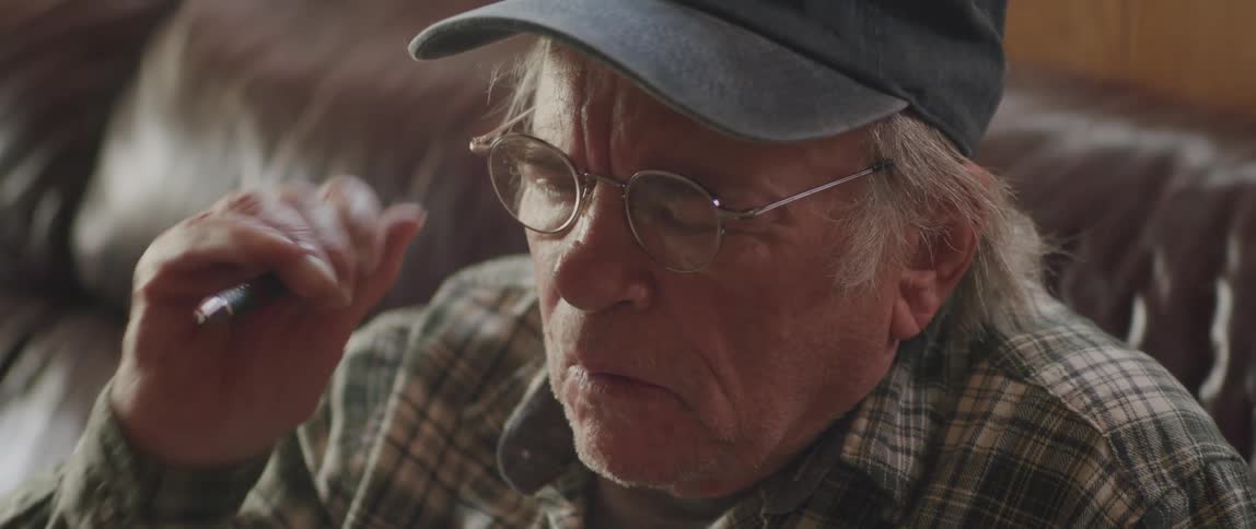 Elderly man sitting taking off his glasses and with a thoughtful facial expression