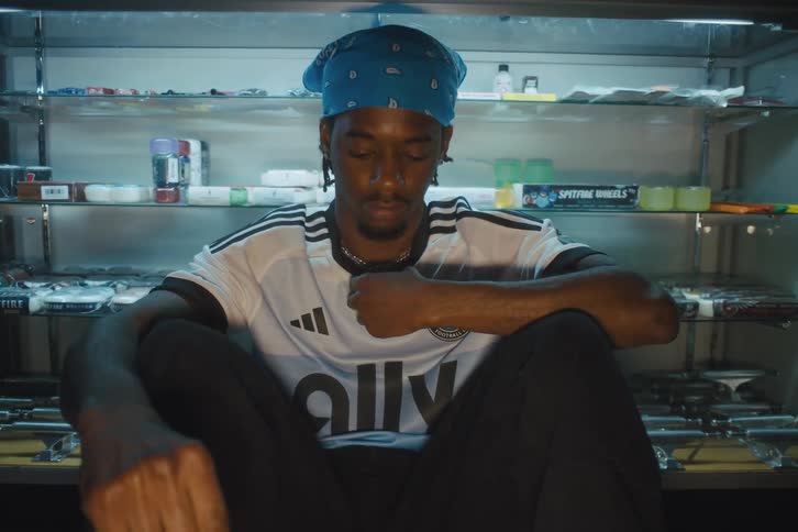 Man sitting adjusting his neck chain and wearing an adidas football shirt
