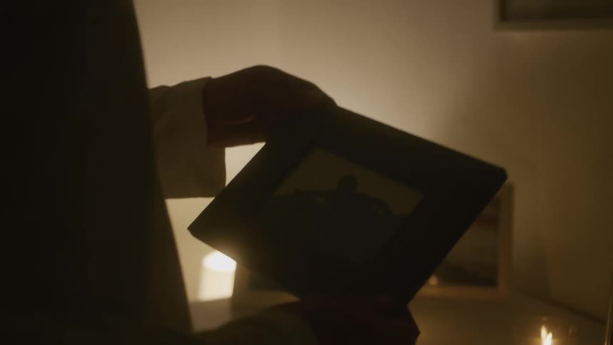 A person illuminated by candle light looking at framed pictures