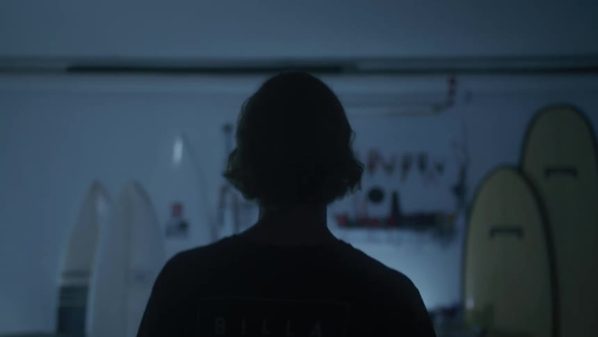 View of a woman from behind walking indoors with surfboards on the wall