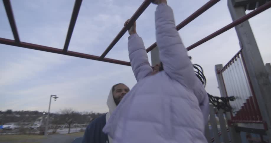 Father next to his daughter who is playing cross a toy with her arms supported and her legs suspended