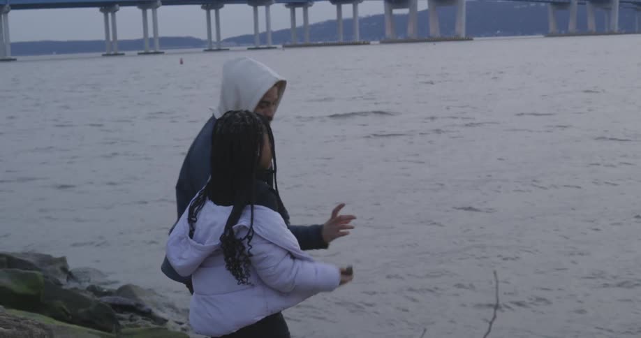 Father teaching her daughter how to skip stones over a lake