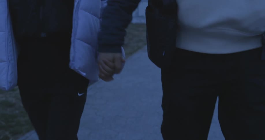 Two people hold hands while walking down the sidewalk