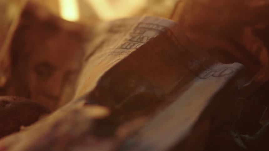 A one hundred dollar bill begins to smolder as its burned by a fire