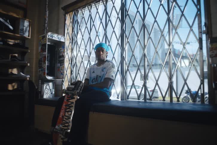 Model man sitting in a store and posing with a soccer club tshirt and a skateboard
