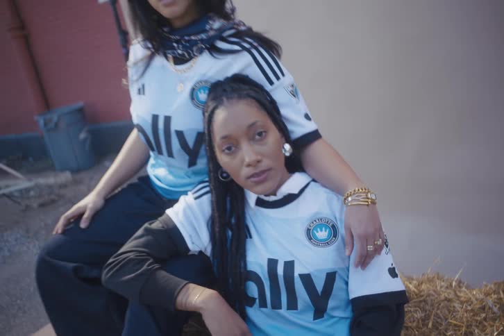 Two young models sitting in a haystack outdoors posing with a football club tshirt
