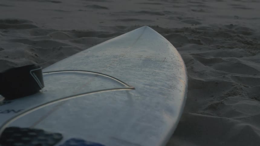 A surfboard is left on the beach with several footprints