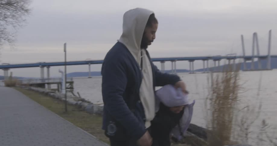 Father putting the hood on his daughter and playing with her as they walk in a square next to the sea