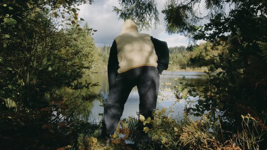 Man holding a leaf looking down at the lake between two trees