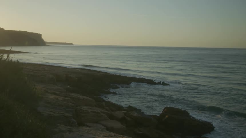 Numerous ocean waves wash upon a rocky coastline under a clear sky