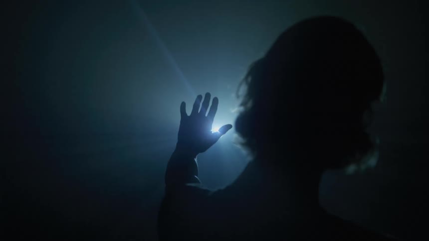 Silhouette of a woman from behind passing her hand through a light clasp
