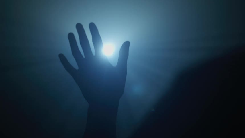Silhouette of a human hand is passing over a bright light in a dark environment