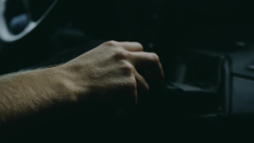 Mans hand gripping the gear shift inside a car