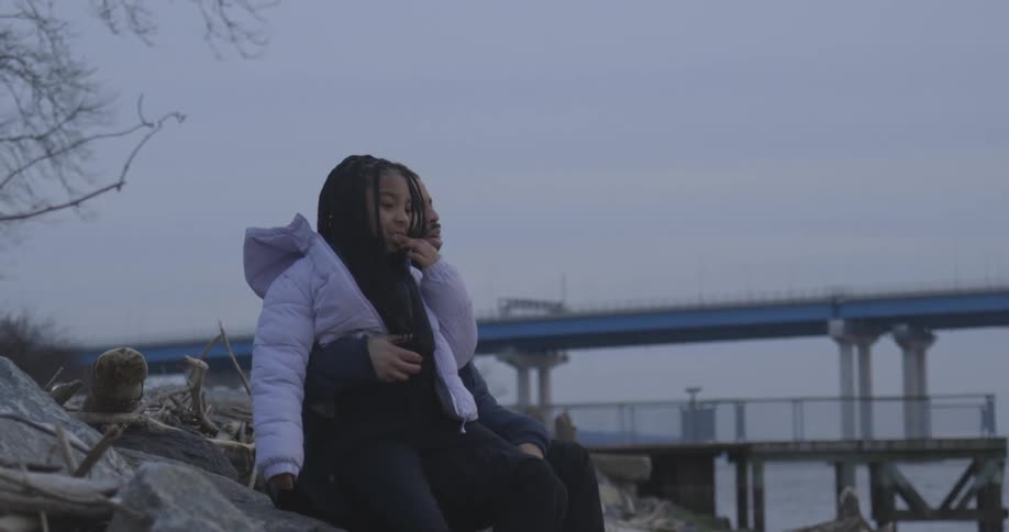 A couple is sitting and wearing warm clothes and they are talking while looking forward and hugging each other