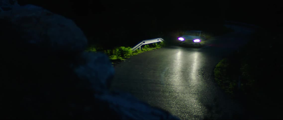 White sedan car making a winding turn down the road at night