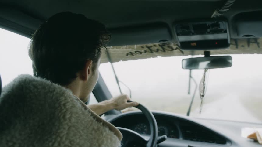 A man holds the steering wheel of his vehicle will driving in the rain