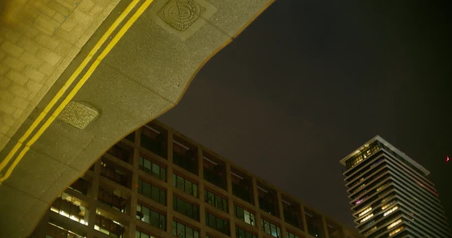 Passing cars are reflectedm in a mirrored roof of a modern buidling