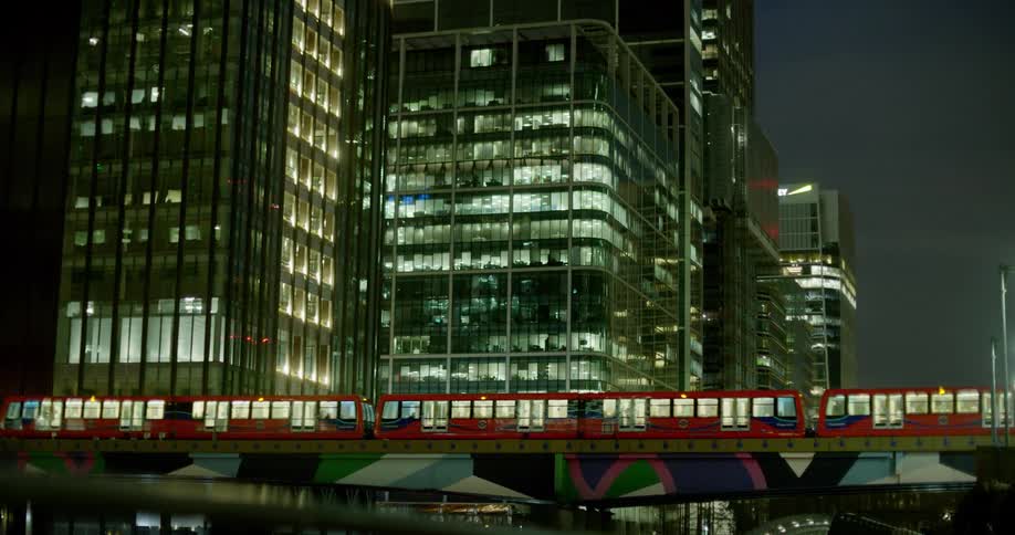 Red public train passing on the viaduct next to buildings in a metropolis at night