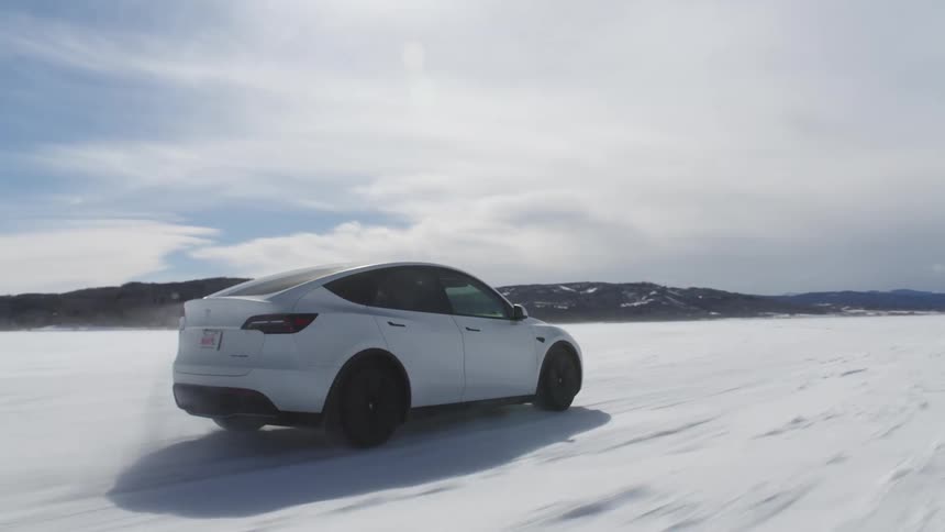 A white car drives over a frozen lake covered in snow