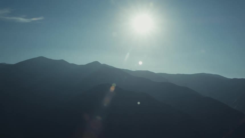 Aerial scenery of rocky mountain ranges and a strong sun on a blue sky day