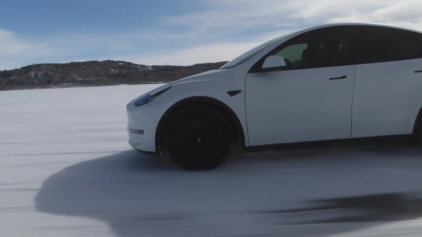 Two people driving a white tesla at high speed on snowcovered ground in a natural environment