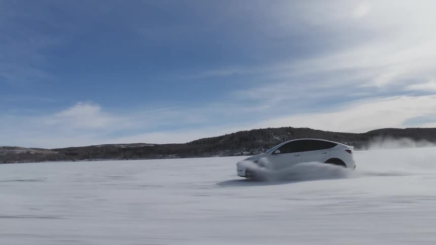 White tesla sports car speeding across snowcovered terrain with mountains on the horizon