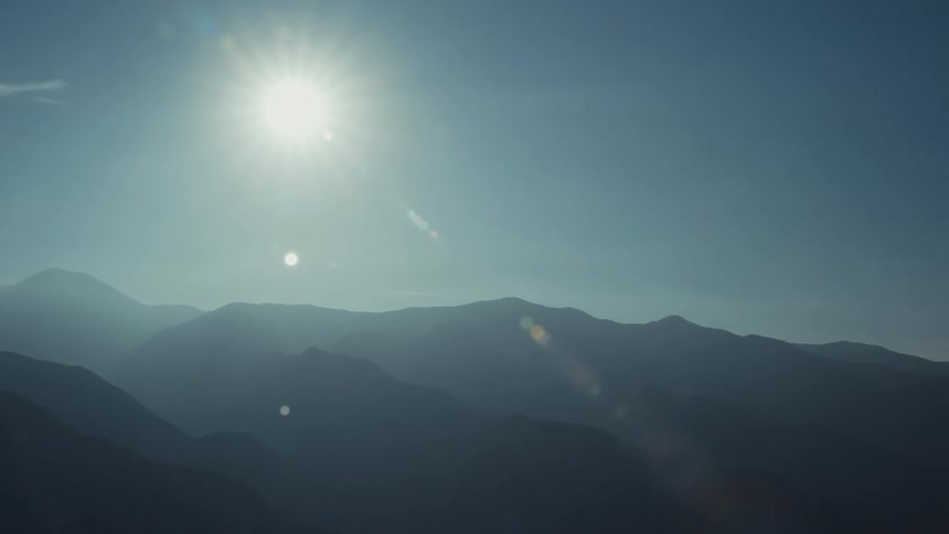 A bright sun shines over a mountain range covered in mist