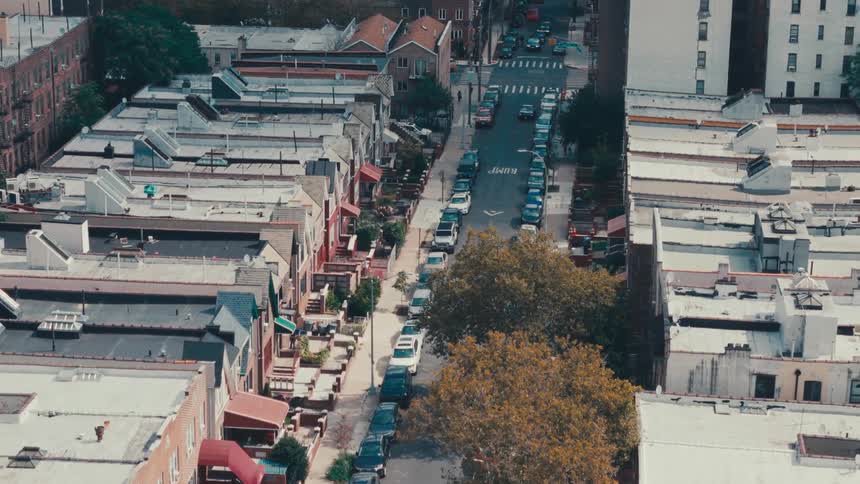 An asphalt street with several cars parked on the sides in an area with many houses and buildings